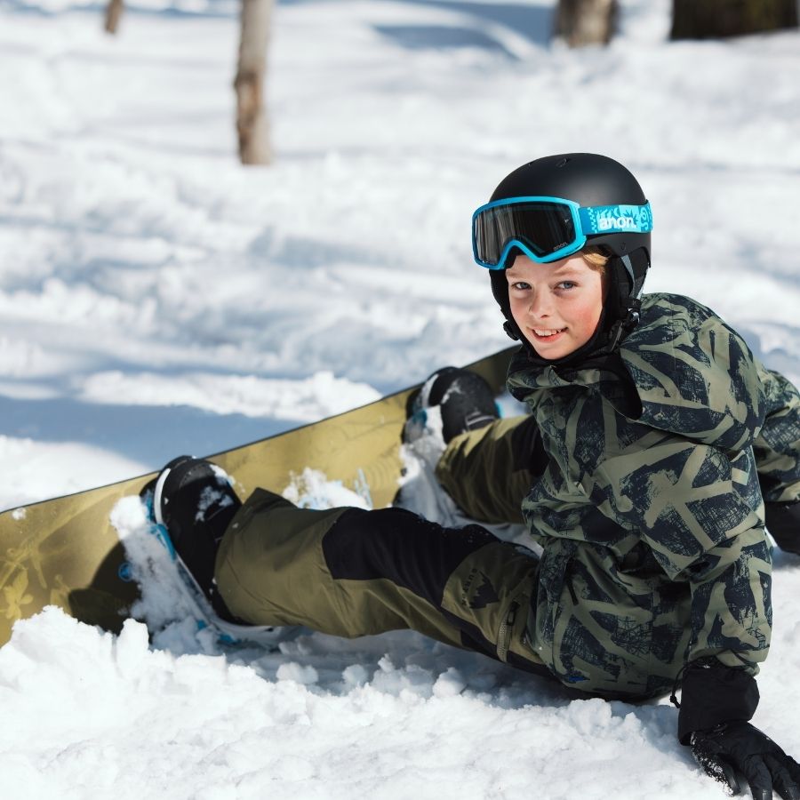 Kind sitzt mit Snowboard mit Bindungen für Kinder im Schnee